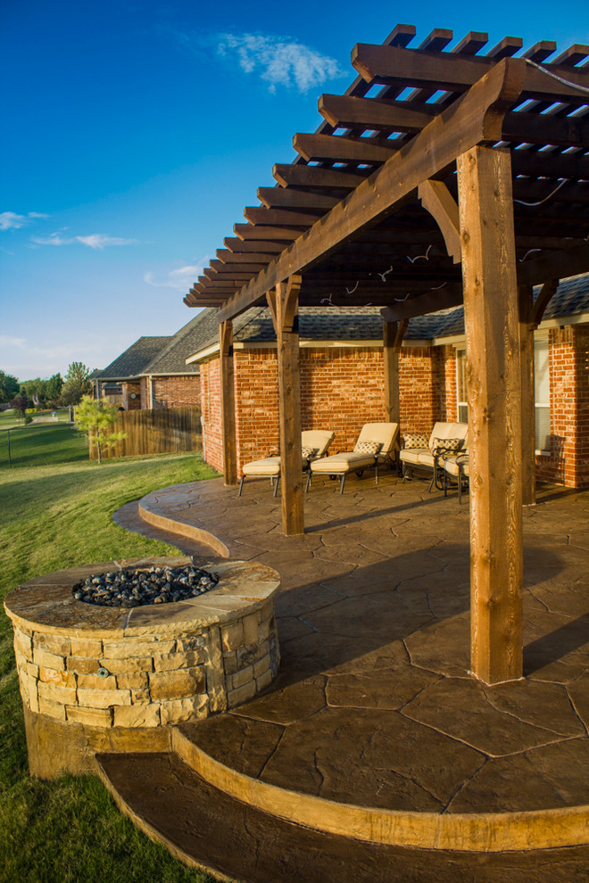 This is an example of a mid-sized arts and crafts backyard patio in Oklahoma City with a fire feature, stamped concrete and a pergola.