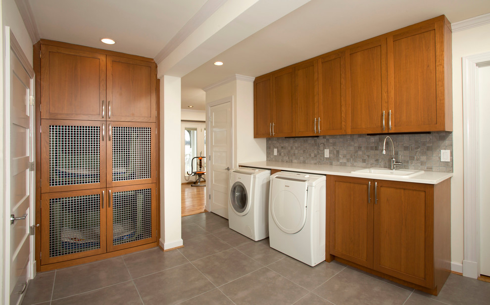 This is an example of a mid-sized transitional l-shaped utility room in DC Metro with a drop-in sink, shaker cabinets, medium wood cabinets, quartz benchtops, a side-by-side washer and dryer, white walls and porcelain floors.