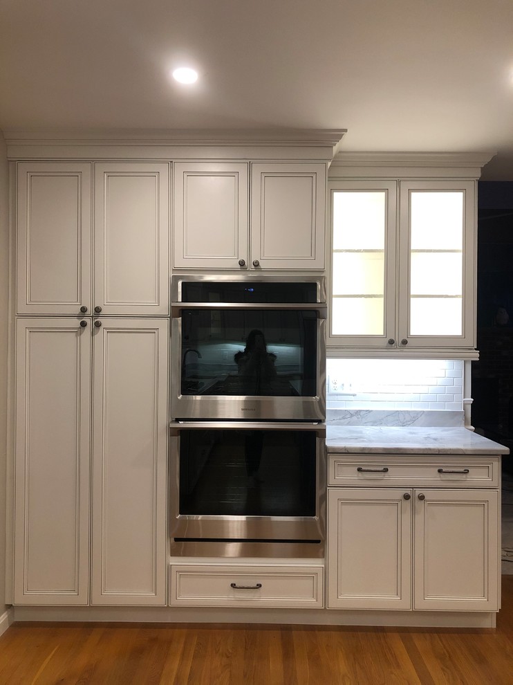 Large transitional l-shaped medium tone wood floor and brown floor open concept kitchen photo in Boston with an undermount sink, recessed-panel cabinets, white cabinets, quartz countertops, white backsplash, subway tile backsplash, stainless steel appliances, an island and multicolored countertops