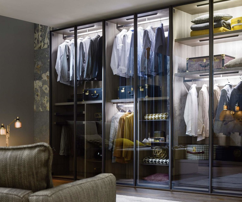 This is an example of a large contemporary gender-neutral walk-in wardrobe in Other with glass-front cabinets, white cabinets, dark hardwood floors and brown floor.