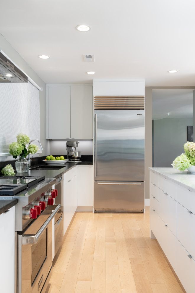 Contemporary u-shaped kitchen in St Louis with an undermount sink, flat-panel cabinets, white cabinets, stainless steel appliances, with island and black benchtop.