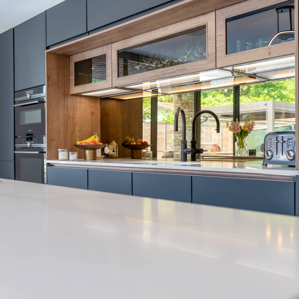Immagine di una grande cucina design con lavello sottopiano, ante con riquadro incassato, ante grigie, top in quarzite, elettrodomestici neri, parquet chiaro, pavimento marrone e top bianco
