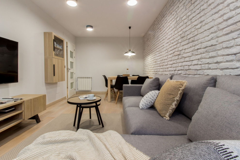 This is an example of a small industrial enclosed living room in Other with grey walls, light hardwood floors, a wall-mounted tv and brick walls.