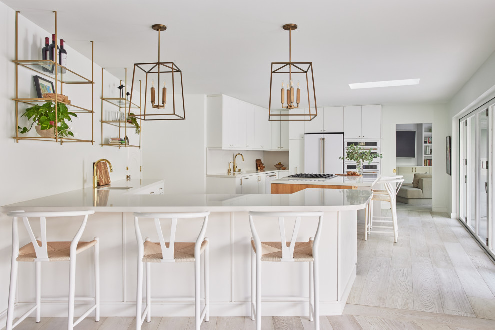 This is an example of a large midcentury u-shaped open plan kitchen in Los Angeles with an undermount sink, flat-panel cabinets, white cabinets, quartz benchtops, white splashback, engineered quartz splashback, white appliances, light hardwood floors, with island, beige floor and white benchtop.