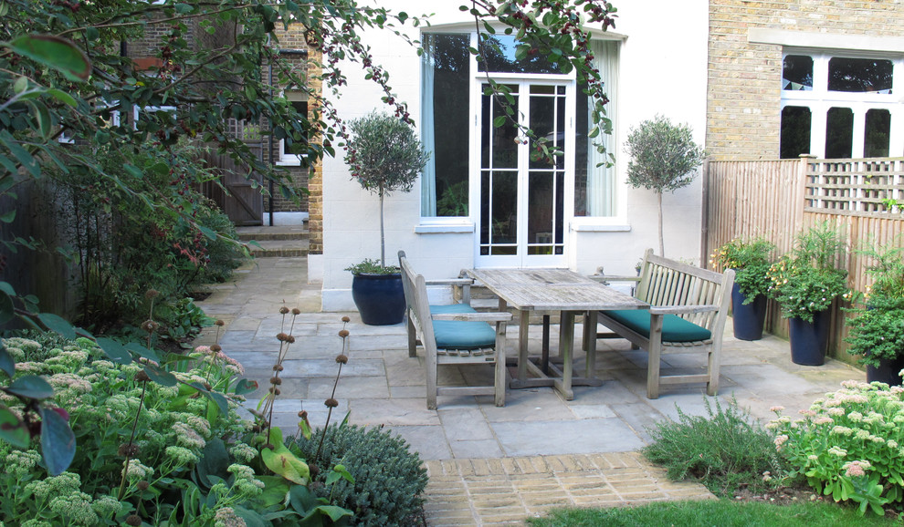 Design ideas for a large traditional backyard patio in London with natural stone pavers.