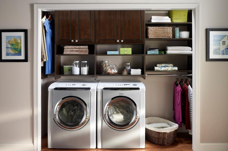 This is an example of a small contemporary single-wall laundry cupboard in Toronto with raised-panel cabinets, dark wood cabinets, beige walls, medium hardwood floors, a side-by-side washer and dryer and brown floor.