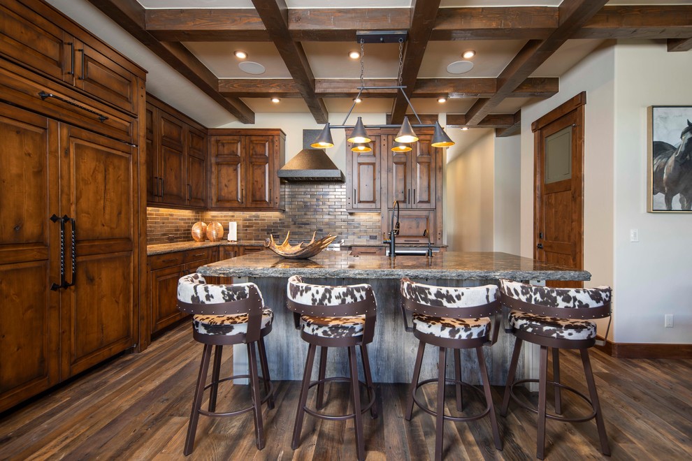 Photo of a country l-shaped kitchen in Denver with raised-panel cabinets, medium wood cabinets, brown splashback, subway tile splashback, dark hardwood floors, with island and grey benchtop.