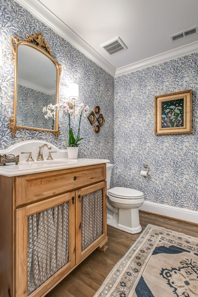 Bathroom in Nashville with open cabinets, light wood cabinets, blue walls, medium hardwood floors, brown floor, a single vanity, a freestanding vanity and wallpaper.