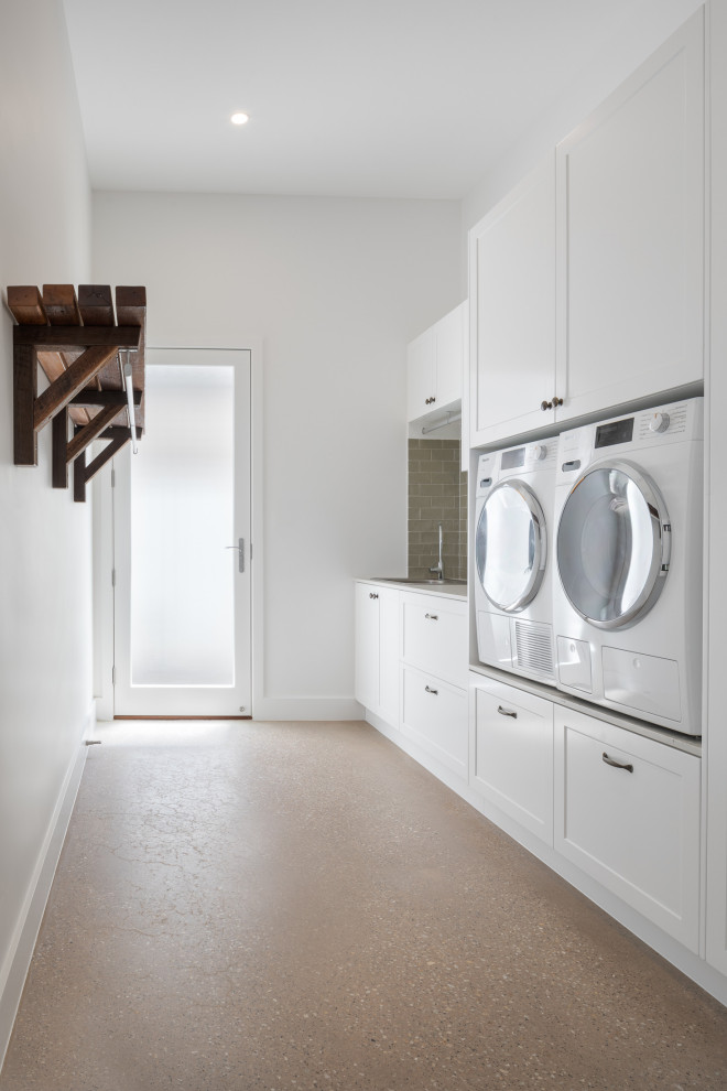 Design ideas for a traditional single-wall dedicated laundry room in Brisbane with a single-bowl sink, shaker cabinets, white cabinets, laminate benchtops, green splashback, subway tile splashback, white walls, concrete floors, a side-by-side washer and dryer and white benchtop.