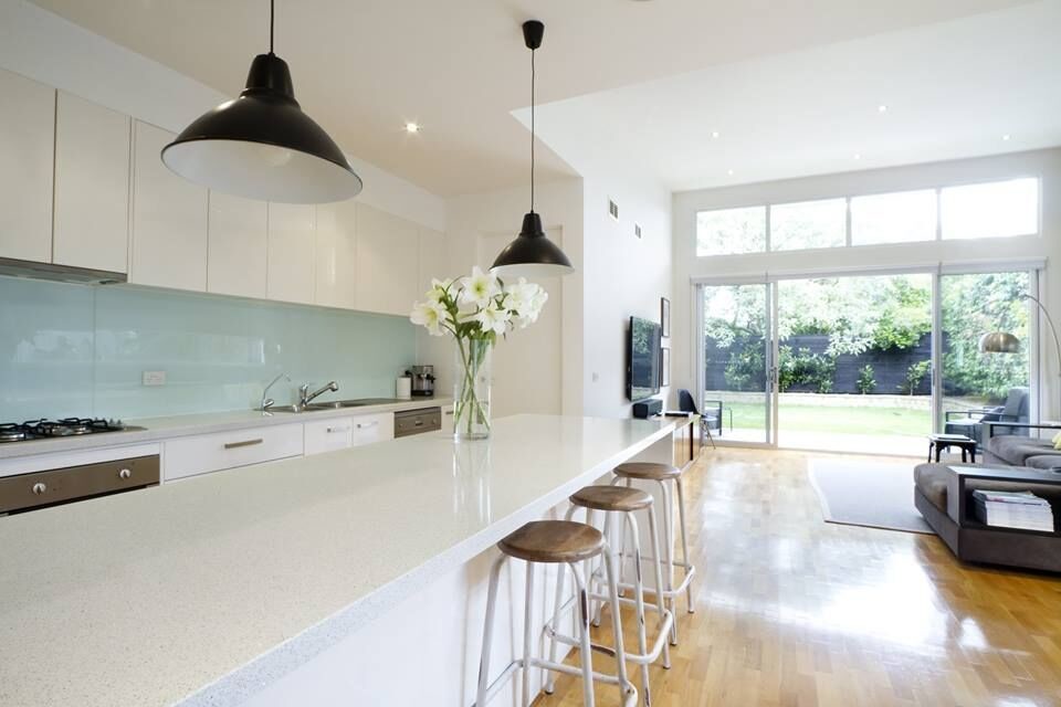 Open concept kitchen - mid-sized transitional single-wall light wood floor and beige floor open concept kitchen idea in Orange County with a double-bowl sink, flat-panel cabinets, white cabinets, glass countertops, blue backsplash, glass sheet backsplash, stainless steel appliances and an island