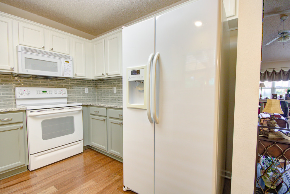 Example of a mid-sized transitional u-shaped medium tone wood floor and brown floor eat-in kitchen design with an undermount sink, shaker cabinets, green cabinets, granite countertops, green backsplash, ceramic backsplash, white appliances, no island and multicolored countertops