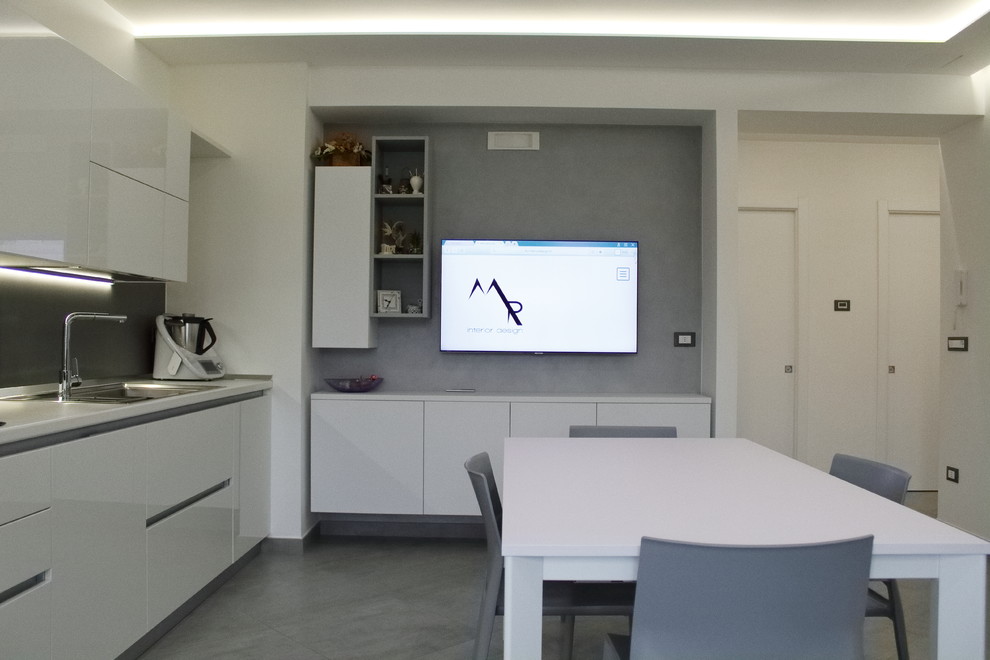 Photo of a mid-sized contemporary single-wall open plan kitchen in Bari with a drop-in sink, flat-panel cabinets, white cabinets, solid surface benchtops, grey splashback, porcelain splashback, stainless steel appliances, porcelain floors, no island, grey floor and white benchtop.