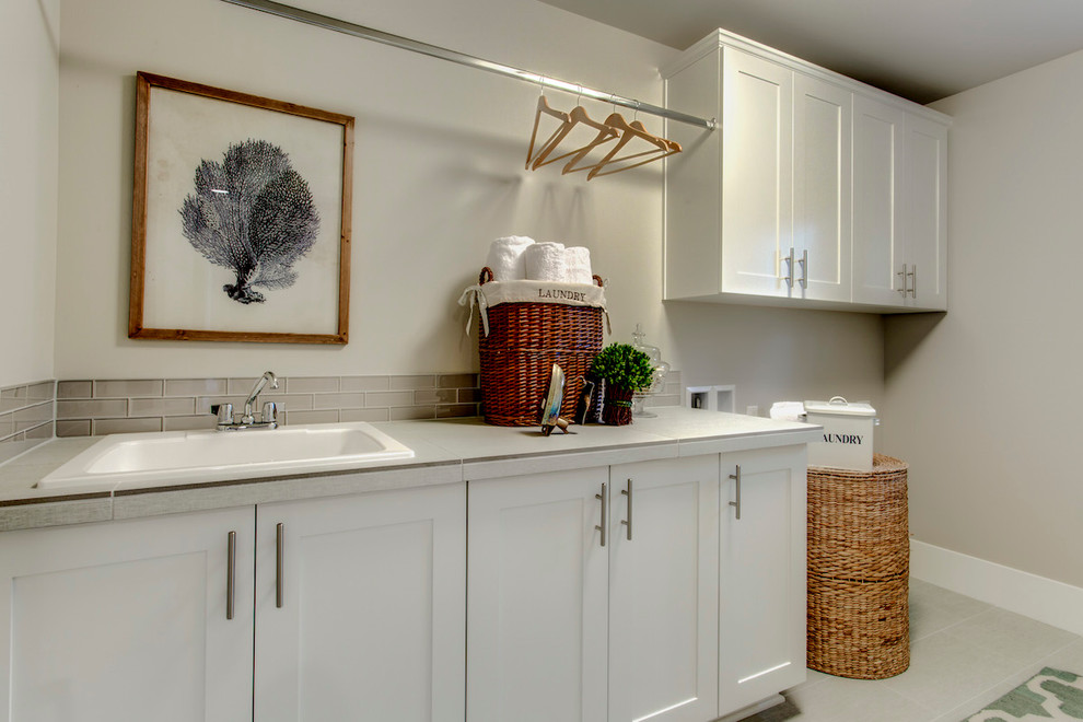 Mid-sized transitional single-wall dedicated laundry room in Seattle with a drop-in sink, raised-panel cabinets, white cabinets, limestone benchtops, grey walls, laminate floors and a side-by-side washer and dryer.