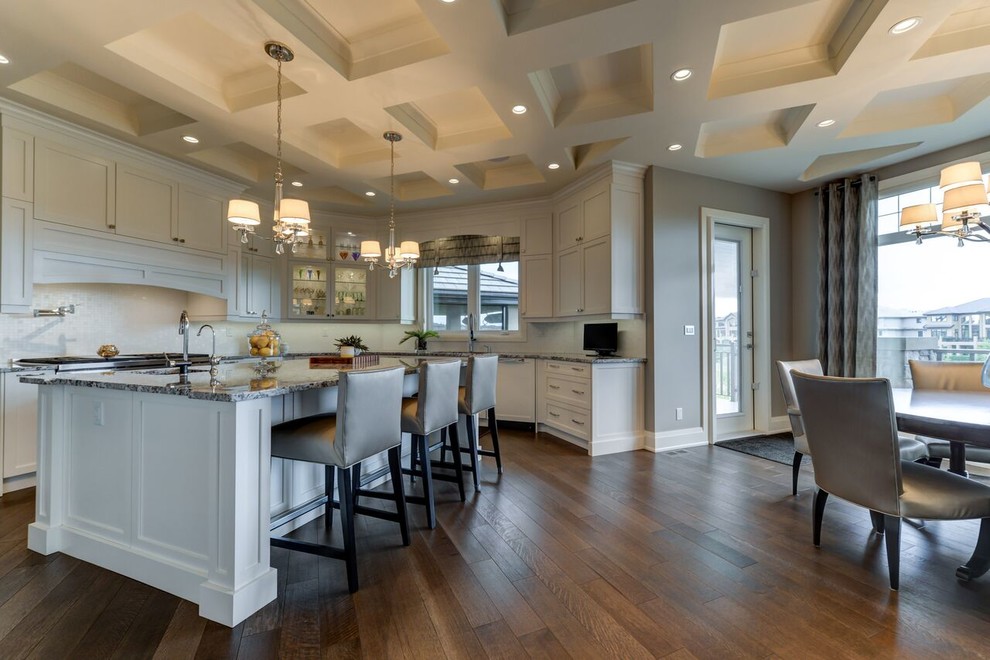 Large transitional u-shaped medium tone wood floor and brown floor kitchen photo in Edmonton with shaker cabinets, white cabinets, granite countertops, white backsplash, an island, an undermount sink, glass tile backsplash and paneled appliances