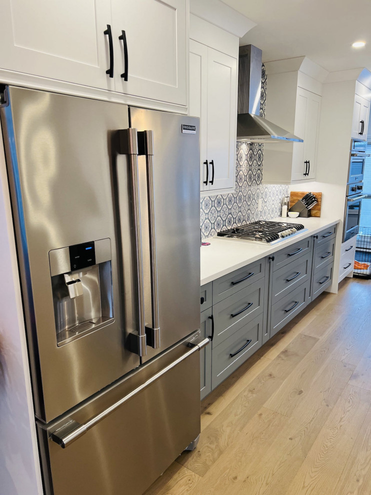 This is an example of a medium sized contemporary galley open plan kitchen in Toronto with a single-bowl sink, shaker cabinets, grey cabinets, engineered stone countertops, blue splashback, cement tile splashback, stainless steel appliances, medium hardwood flooring, an island, brown floors and white worktops.