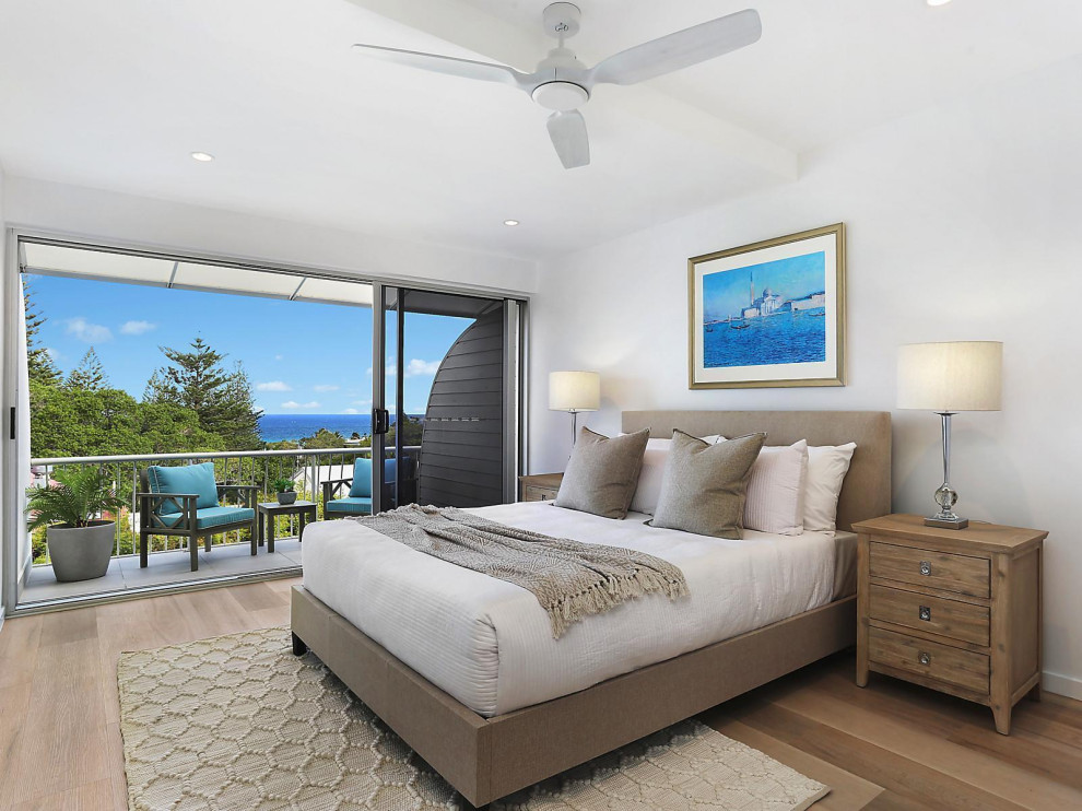 Large mediterranean master bedroom in Sunshine Coast with white walls, medium hardwood floors and brown floor.