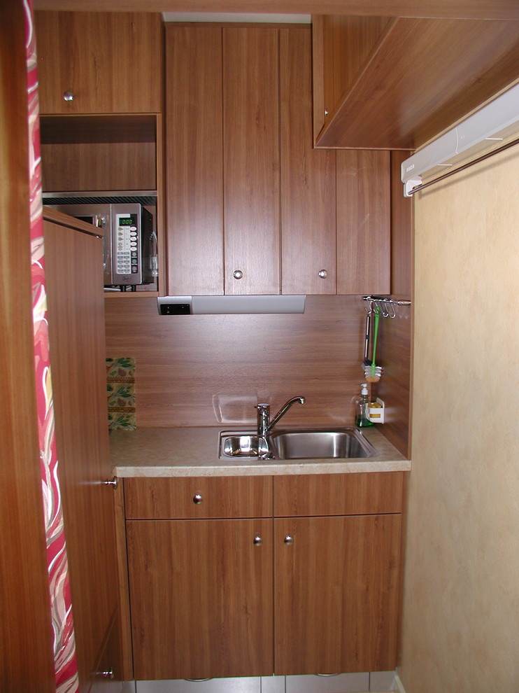 This is an example of a small modern l-shaped separate kitchen in Frankfurt with flat-panel cabinets, brown cabinets, wood benchtops, no island, a drop-in sink, brown splashback, timber splashback, stainless steel appliances, beige benchtop and ceramic floors.