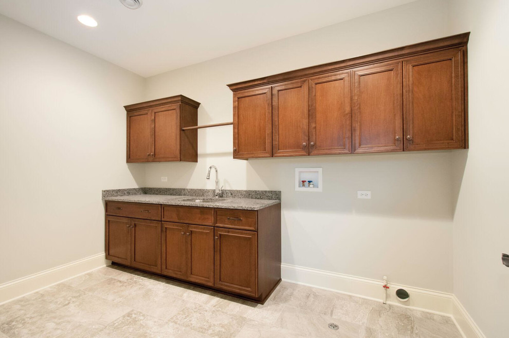 This is an example of a mid-sized transitional single-wall dedicated laundry room in Chicago with an undermount sink, raised-panel cabinets, dark wood cabinets, granite benchtops, grey walls, ceramic floors, a side-by-side washer and dryer and grey floor.