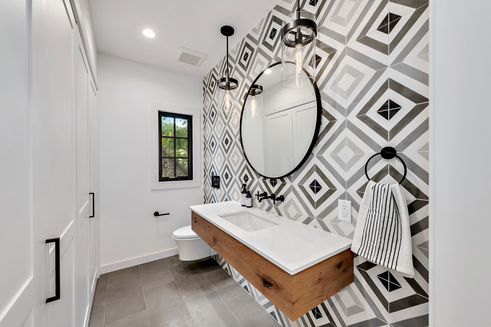 Transitional powder room in New York with flat-panel cabinets, medium wood cabinets, a wall-mount toilet, black and white tile, gray tile, white walls, an undermount sink and grey floor.