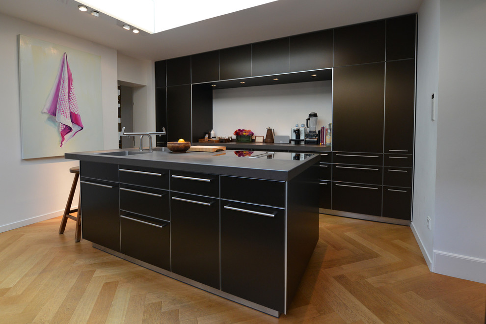 Mid-sized contemporary kitchen in Dusseldorf with flat-panel cabinets, black cabinets, panelled appliances, light hardwood floors, with island and an integrated sink.