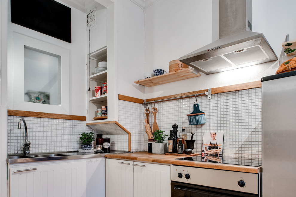 This is an example of a small scandinavian separate kitchen in Gothenburg with wood benchtops, grey splashback, stainless steel appliances, light hardwood floors and no island.