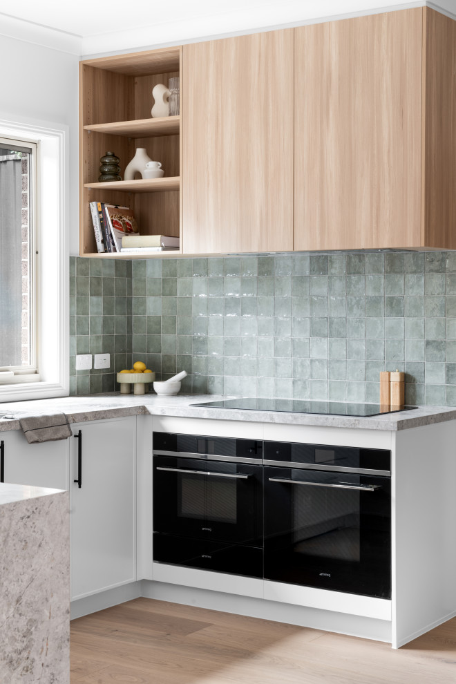 Photo of an u-shaped kitchen in Melbourne with a double-bowl sink, shaker cabinets, white cabinets, marble benchtops, green splashback, porcelain splashback, black appliances, a peninsula and grey benchtop.