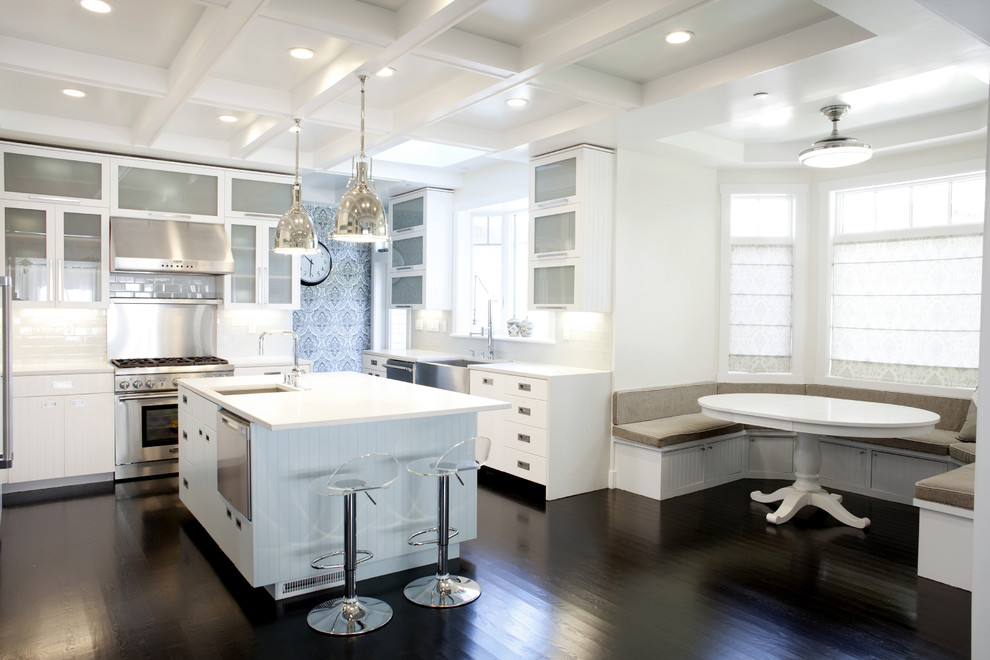 Inspiration for a mid-sized transitional l-shaped eat-in kitchen in San Francisco with stainless steel appliances, glass-front cabinets, white cabinets, white splashback, subway tile splashback, dark hardwood floors, with island, brown floor and a farmhouse sink.