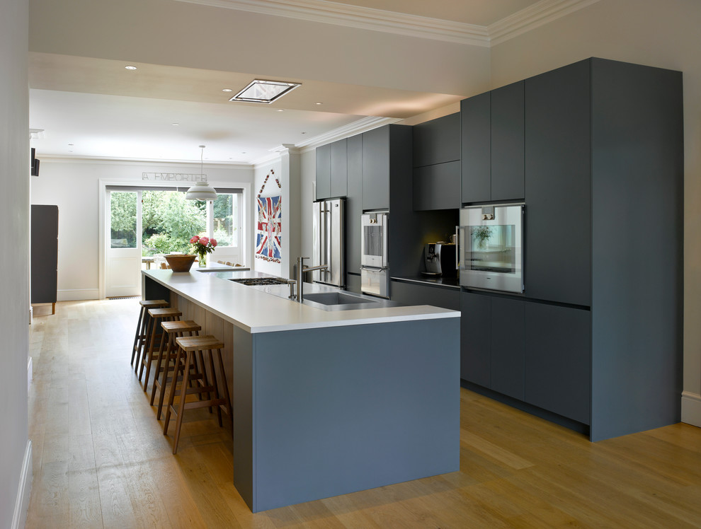 Large contemporary open plan kitchen in London with an undermount sink, flat-panel cabinets, blue cabinets, solid surface benchtops and with island.