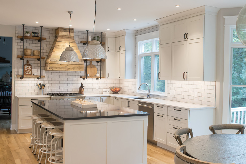 Design ideas for a large country u-shaped eat-in kitchen in Grand Rapids with an undermount sink, shaker cabinets, white cabinets, quartz benchtops, white splashback, subway tile splashback, stainless steel appliances, light hardwood floors, with island and brown floor.