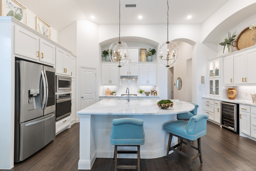 Inspiration for a transitional u-shaped medium tone wood floor and brown floor kitchen remodel in Dallas with a farmhouse sink, shaker cabinets, white cabinets, marble countertops, gray backsplash, an island and multicolored countertops