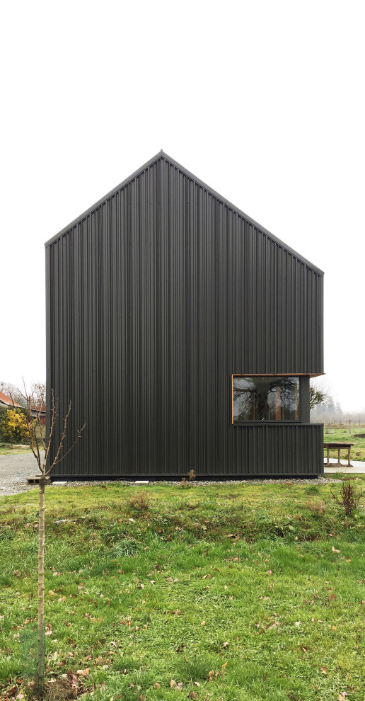 Cette image montre une très grande façade de maison métallique et noire design à deux étages et plus avec un toit à deux pans, un toit en métal et un toit gris.