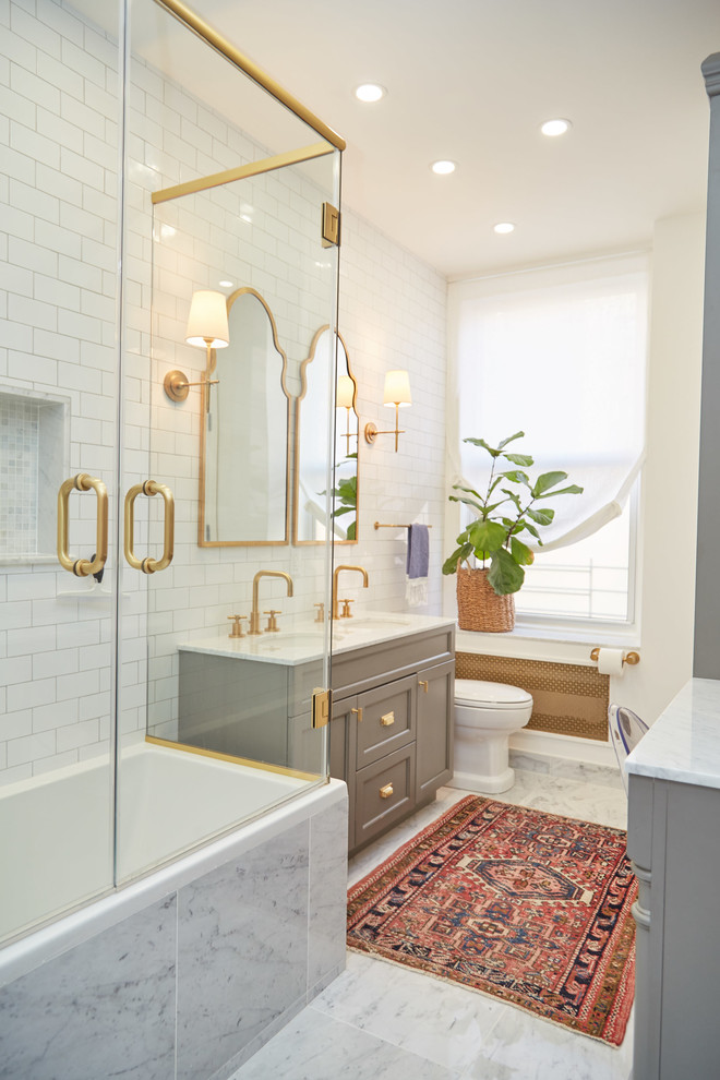 Photo of a transitional master bathroom in New York with recessed-panel cabinets, grey cabinets, a drop-in tub, a shower/bathtub combo, white tile, white walls, an undermount sink, grey floor and a hinged shower door.