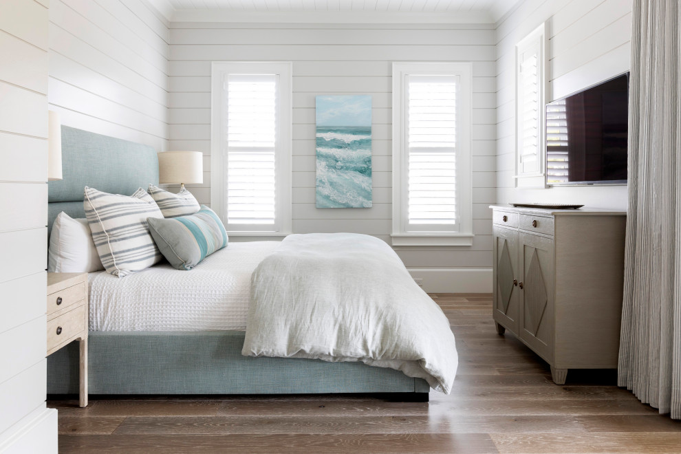 Modelo de dormitorio principal costero grande con paredes blancas, suelo de madera clara, suelo marrón, casetón y machihembrado