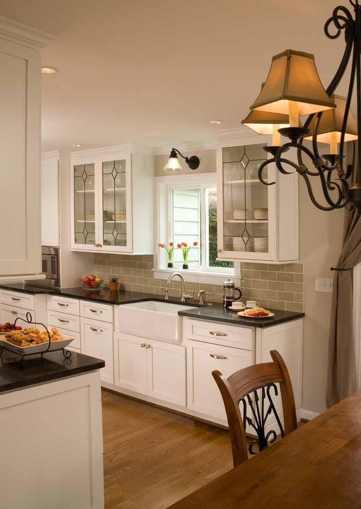 Eat-in kitchen - traditional galley medium tone wood floor eat-in kitchen idea in Seattle with a farmhouse sink, shaker cabinets, white cabinets, green backsplash, subway tile backsplash, stainless steel appliances and beige walls