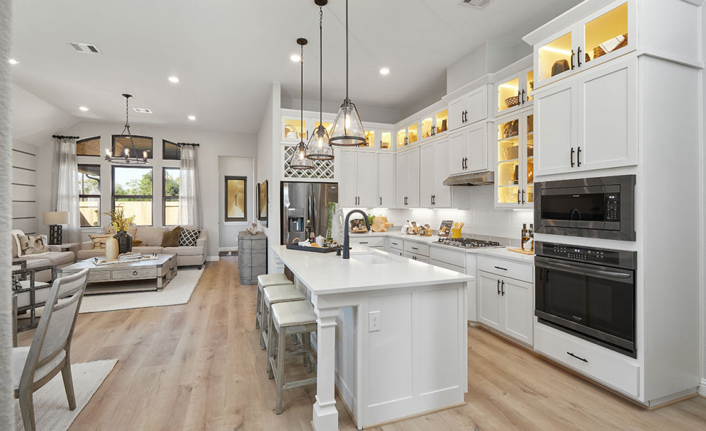 Contemporary l-shaped open plan kitchen in Houston with a single-bowl sink, recessed-panel cabinets, white cabinets, white splashback, ceramic splashback, stainless steel appliances, laminate floors, with island, brown floor and white benchtop.