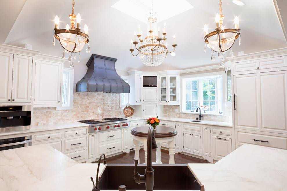 Photo of a traditional l-shaped kitchen in Milwaukee with a farmhouse sink, raised-panel cabinets, white cabinets, beige splashback, stone tile splashback and panelled appliances.