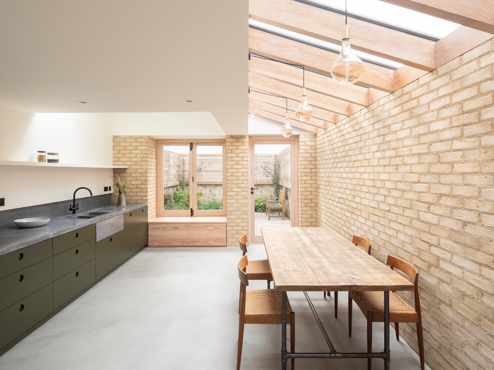 This is an example of a mid-sized single-wall eat-in kitchen in London with a drop-in sink, flat-panel cabinets, green cabinets, concrete benchtops, grey splashback, stone slab splashback, black appliances, concrete floors, no island, grey floor and grey benchtop.