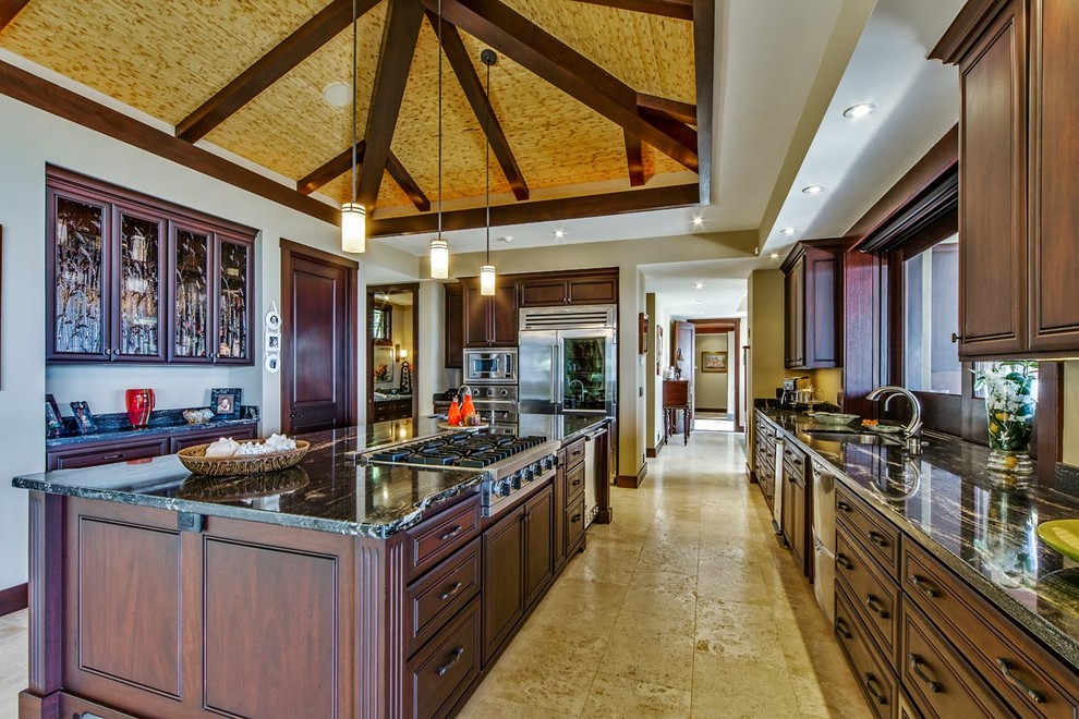 Inspiration for a large tropical u-shaped open plan kitchen in Hawaii with an undermount sink, raised-panel cabinets, brown cabinets, granite benchtops, black splashback, stone slab splashback, stainless steel appliances, travertine floors and with island.