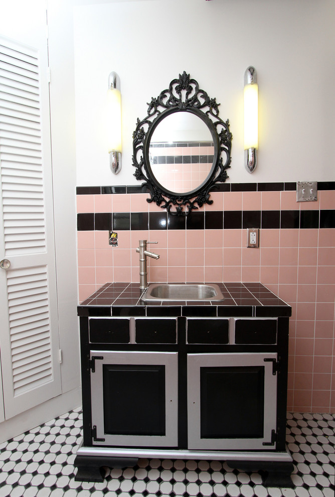 Photo of a small midcentury 3/4 bathroom in New York with a drop-in sink, recessed-panel cabinets, black cabinets, tile benchtops, a corner tub, a two-piece toilet, black tile, ceramic tile, pink walls and mosaic tile floors.