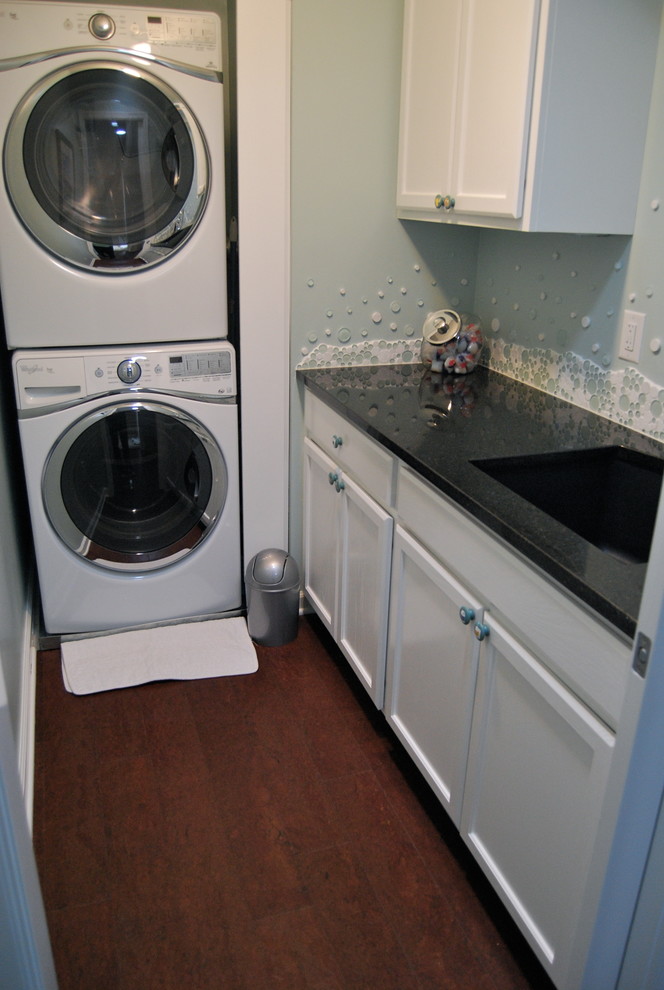 Photo of a mid-sized traditional l-shaped dedicated laundry room in Kansas City with a single-bowl sink, recessed-panel cabinets, white cabinets, granite benchtops, blue walls, cork floors and a stacked washer and dryer.