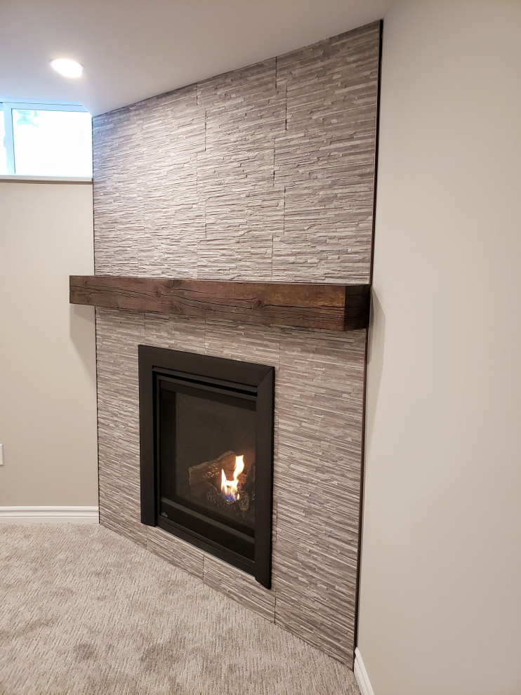 Design ideas for a mid-sized transitional look-out basement in Toronto with beige walls, carpet, a corner fireplace, a tile fireplace surround and grey floor.