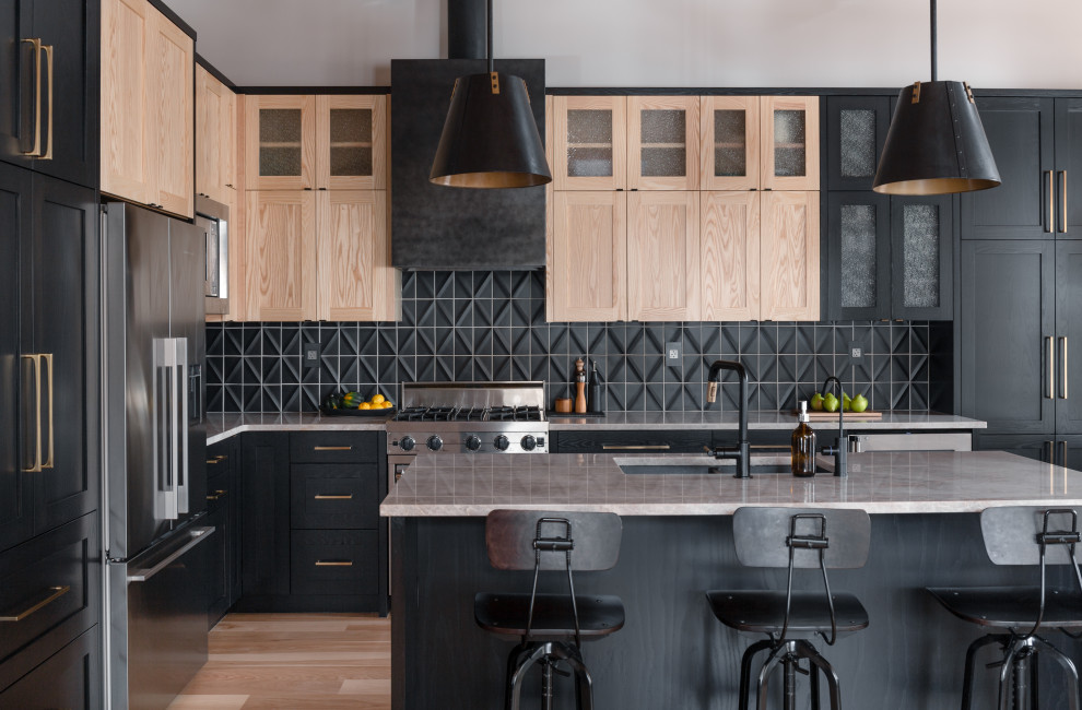 Photo of a large transitional l-shaped eat-in kitchen in Other with a double-bowl sink, shaker cabinets, black cabinets, quartzite benchtops, black splashback, ceramic splashback, stainless steel appliances, light hardwood floors, with island, brown floor, grey benchtop and exposed beam.
