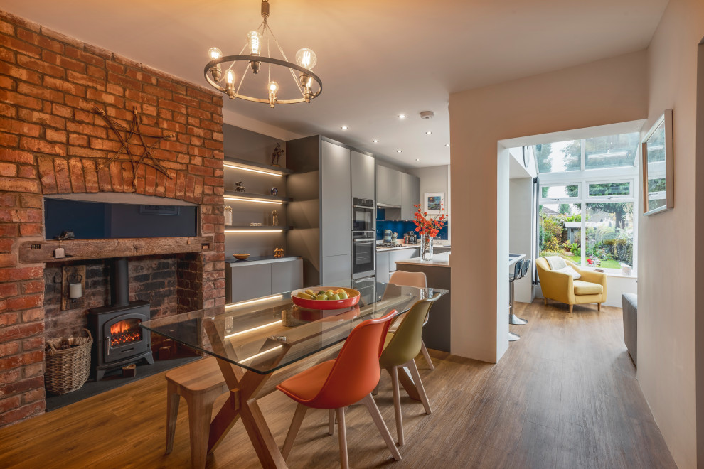 Mid-sized contemporary kitchen/dining combo in Manchester with white walls, medium hardwood floors, a wood stove, a brick fireplace surround and brown floor.