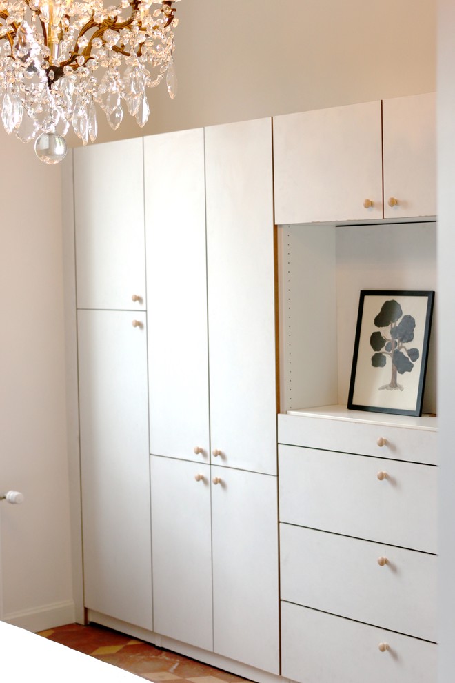 Inspiration for a mid-sized transitional gender-neutral built-in wardrobe in Paris with flat-panel cabinets, white cabinets, terra-cotta floors and orange floor.