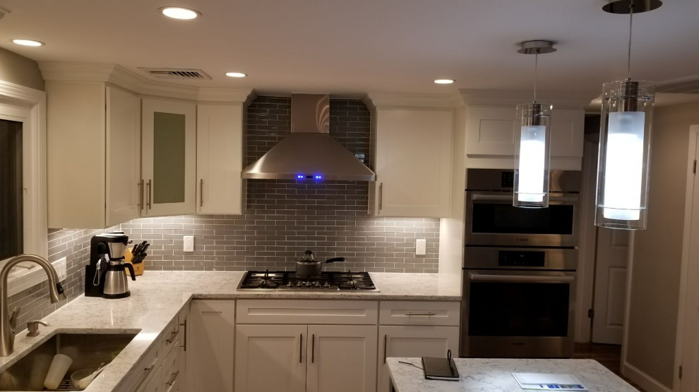 Mid-sized transitional l-shaped dark wood floor and brown floor open concept kitchen photo with an undermount sink, shaker cabinets, white cabinets, gray backsplash, stainless steel appliances, an island and white countertops