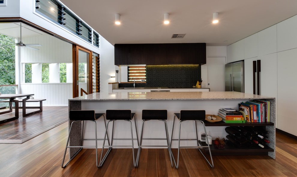 This is an example of a contemporary galley open plan kitchen in Brisbane with an undermount sink, white cabinets, quartz benchtops, grey splashback, metal splashback, stainless steel appliances, medium hardwood floors and with island.