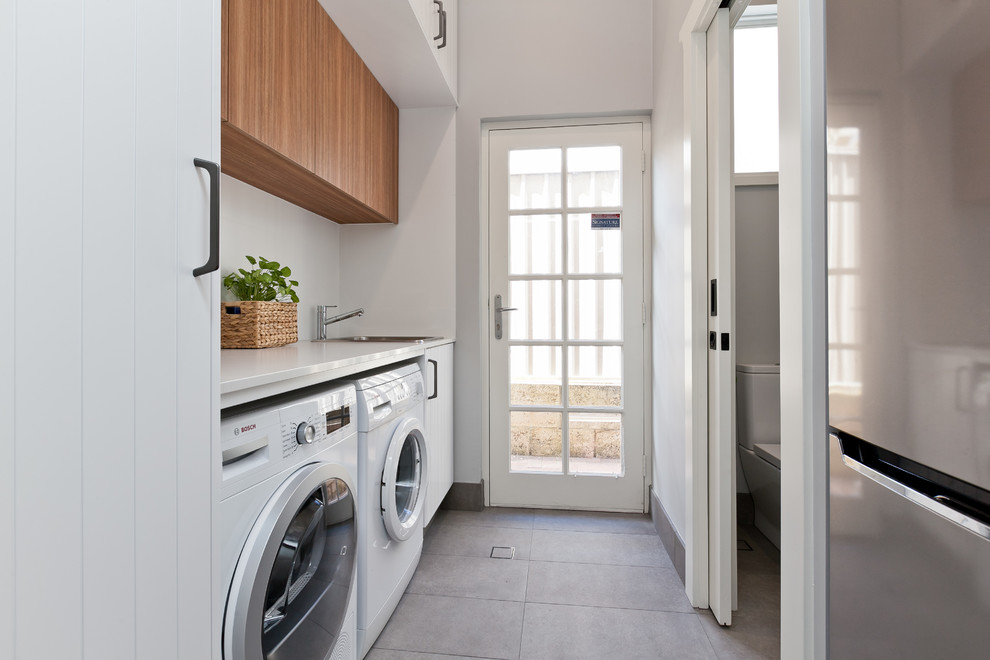 Inspiration for a small contemporary galley dedicated laundry room in Perth with a drop-in sink, white cabinets, quartz benchtops, grey walls, porcelain floors, a side-by-side washer and dryer, grey floor, white benchtop and flat-panel cabinets.
