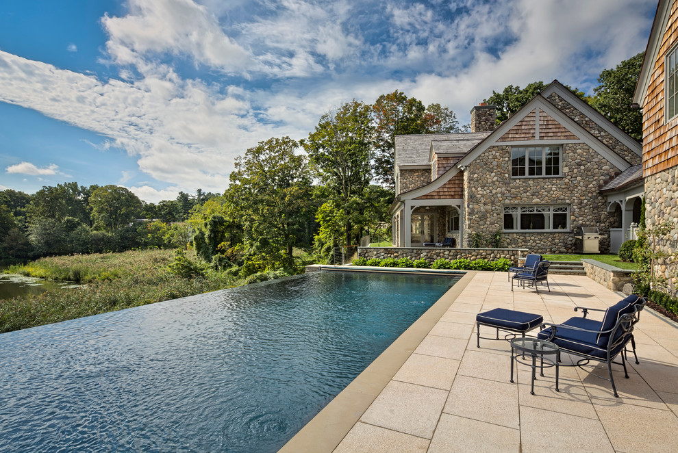 Photo of an expansive transitional backyard rectangular infinity pool in New York with a pool house and concrete pavers.