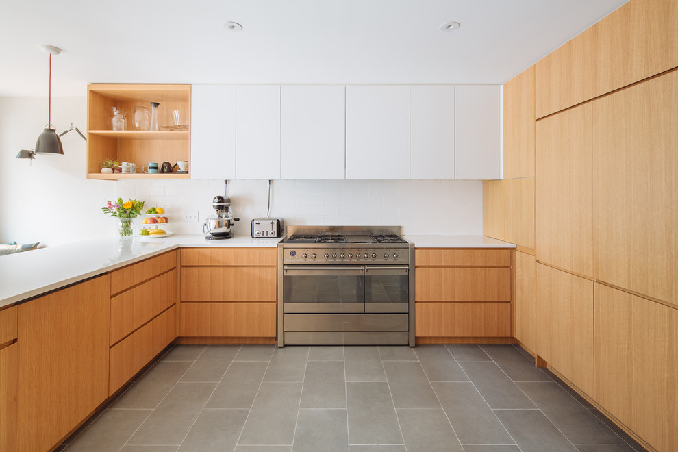 Contemporary kitchen in New York with flat-panel cabinets, light wood cabinets, white splashback, stainless steel appliances, a peninsula and grey floor.