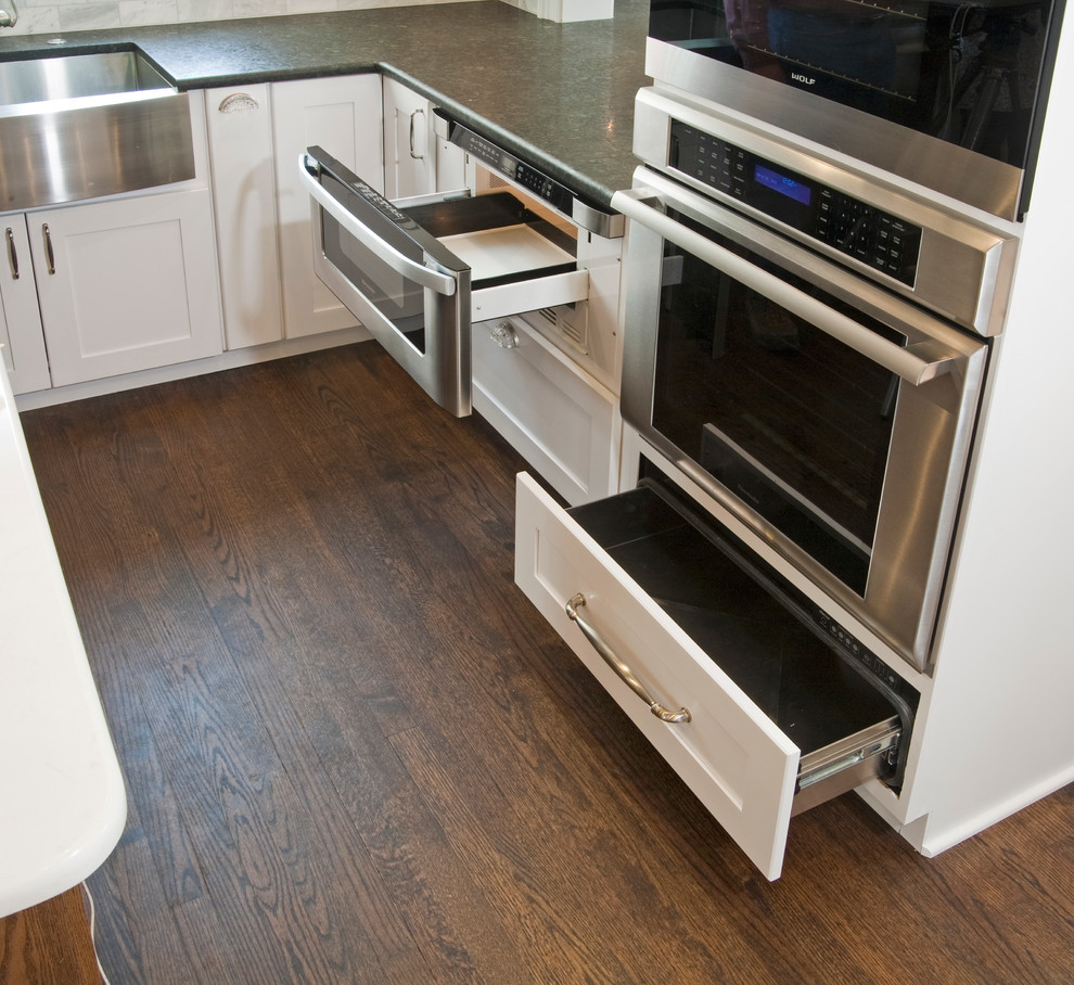 Eat-in kitchen - large transitional l-shaped medium tone wood floor eat-in kitchen idea in Philadelphia with a farmhouse sink, shaker cabinets, white cabinets, granite countertops, gray backsplash, stone tile backsplash, stainless steel appliances and an island
